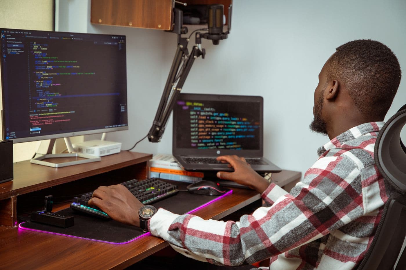 A developer writing code at a desk with a monitor and a laptop