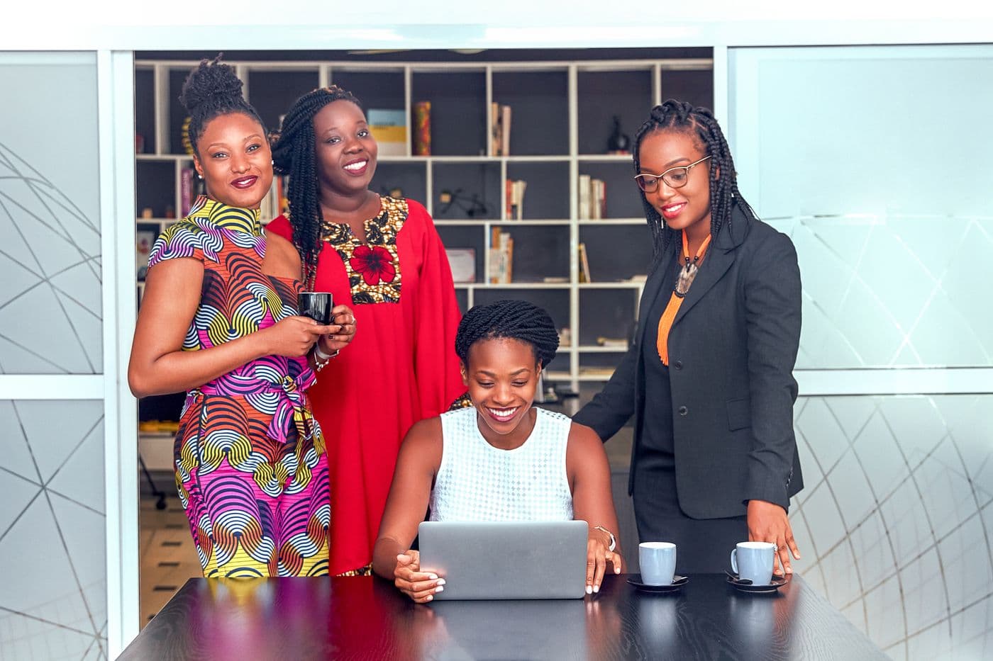 Four women gathered around a laptop in an office, smiling